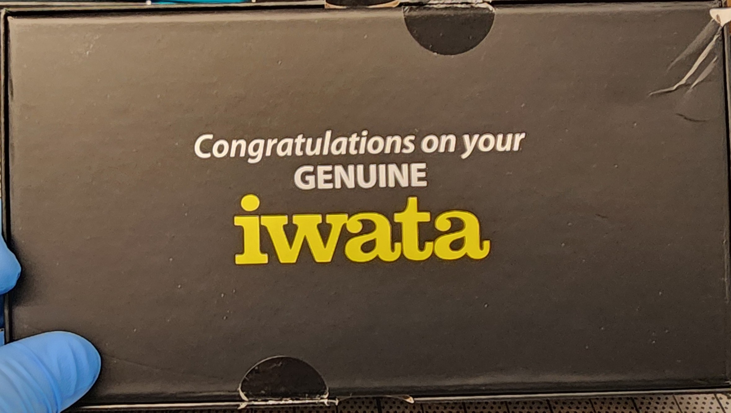 Bottom of the black eclipse cs box showing 2 .75 inch clear circle seals applied to the lower spine just left of middle and the upper spine just right of middle, when the iwata logo is positioned correctly