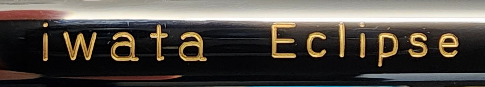 Closeup of a bright, glowing brass engraving that reads Iwata Eclipse on the side of an airbrush